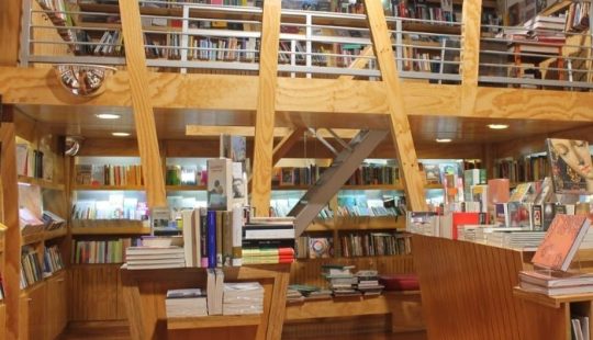 Fotografía de una de las Librerías UC por dentro, se ven muchas vigas de madera y estantes, con cientos de libros