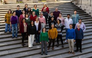 Fotografía de parte de los miembros del Coro Alumni UC vestidos de distintos colores en una gran escalera amplia