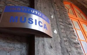 Fotografía de una pared de cemento con una ventana roja y un cartel escrito Instituto de Música