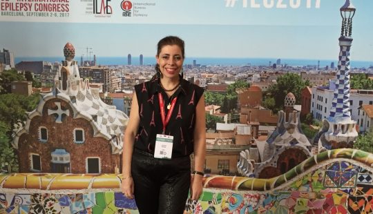 Fotografía de la egresada UC, Keryma Acevedo, con el afiche de un Congreso de fondo