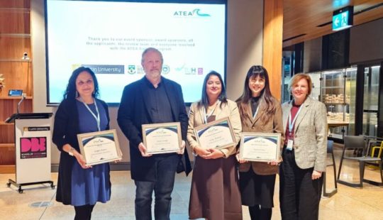 Fotografía de un grupo de cinco personas posando en una ceremonia, sosteniendo certificados.