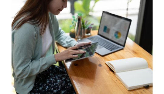 Imagen de una mujer usando una tablet con una laptop de fondo
