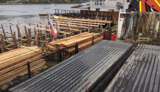 Fotografía de casas en construcción en una zona de palafitos, se ve la bandera de Chile