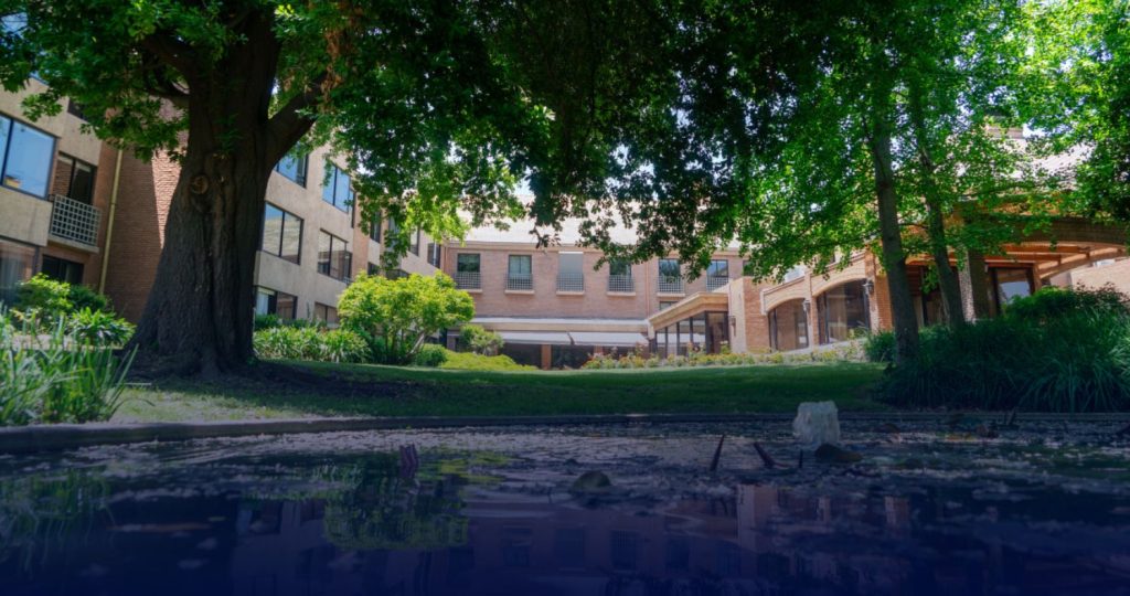 Fotografía de una sede de Senior suits, se ve de fondo un gran edificio y frente a éste mucho verde y una pequeña laguna