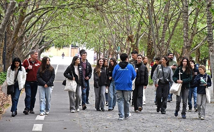 Fotografía de una veintena de personas en la arboleda del Campus San Joaquín UC junto a un embajador que lleva su tradicional cortavientos azul