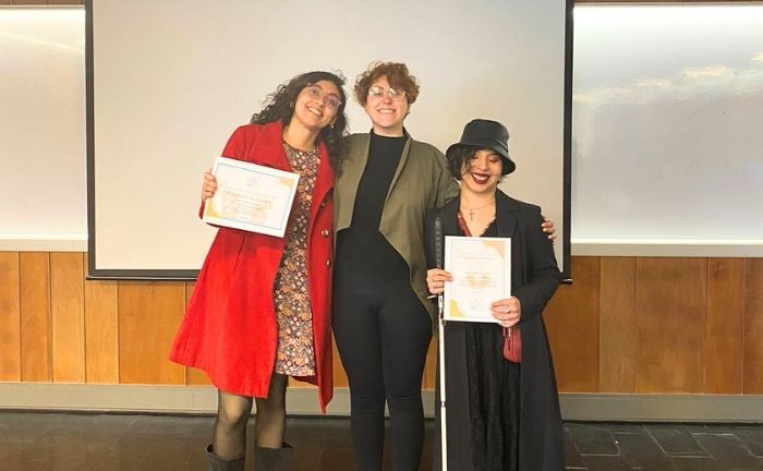 Fotografía de tres mujeres de pie sonriendo, dos de ellas sostienen un diploma, una de ellas sujeta un bastón para personas ciegas