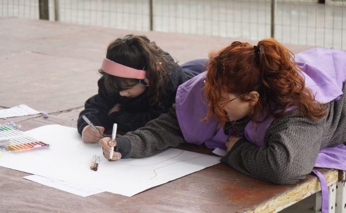 Dos personas, una adulta y una niña, sentadas escribiendo en un papelógrafo, no se ven sus rostros