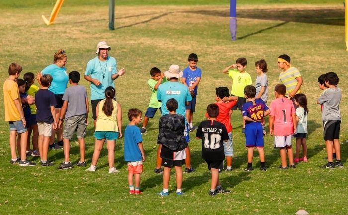 Fotografía de un grupo de decenas de niños y niñas junto a monitores en una cancha de pasto