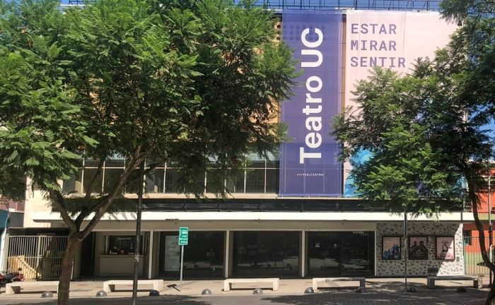 Fotografía del frontis del Teatro UC, se ve un gran telón con el nombre del teatro, y a un costado escrito "Estar, mirar, sentir"