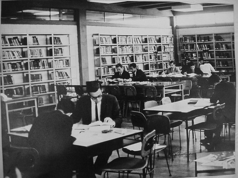 Fotografía en blanco y negro de personas con terno en una biblioteca