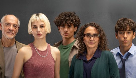 Fotografía de cinco personas de distintas edades posando frente a un fondo neutro.