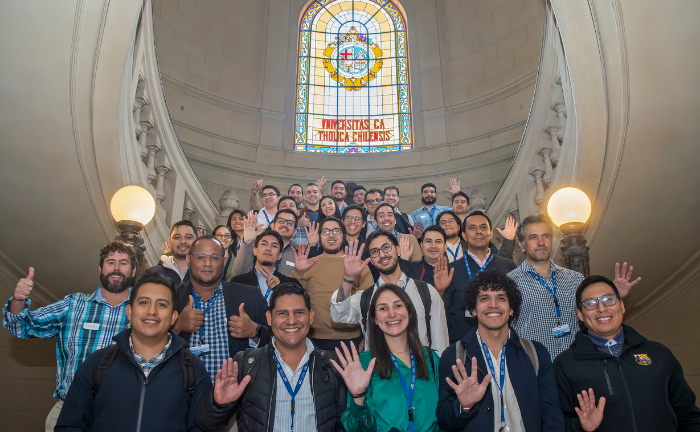 Fotografía de un grupo de decenas de personas sonriendo y alcanzo la palma de la mano