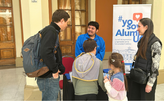 Fotografía de un stand con u pendón con #YoSoyAlumniUC y una familia