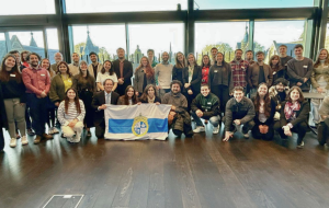 Fotografía de un grupo de decenas de personas al centro algunas sosteniendo la bandera de la Universidad Católica