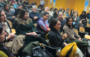 Fotografía de decenas de personas en un auditorio una de ellas con un micrófono